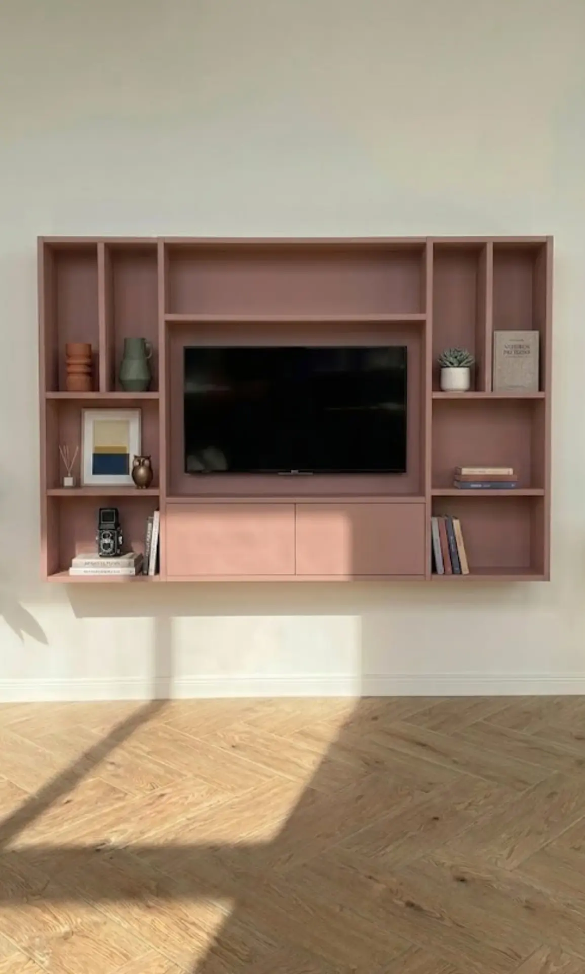 Roze cinewall met tv en vakken in lichte woonkamer